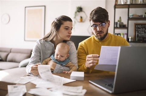 man and woman working on expenses on laptop while holding a baby