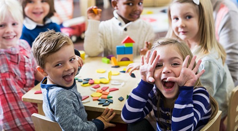 A group of children in a classroom doing crafts and smiling at camera