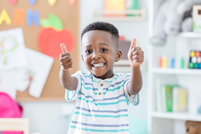 A young black child smiling with both arms extended forward with each hand giving a 